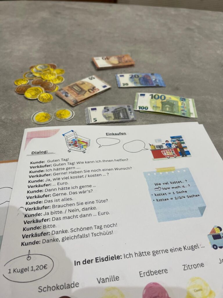 German shopping role play with a dialogue worksheet, play notes and coins on the classroom table