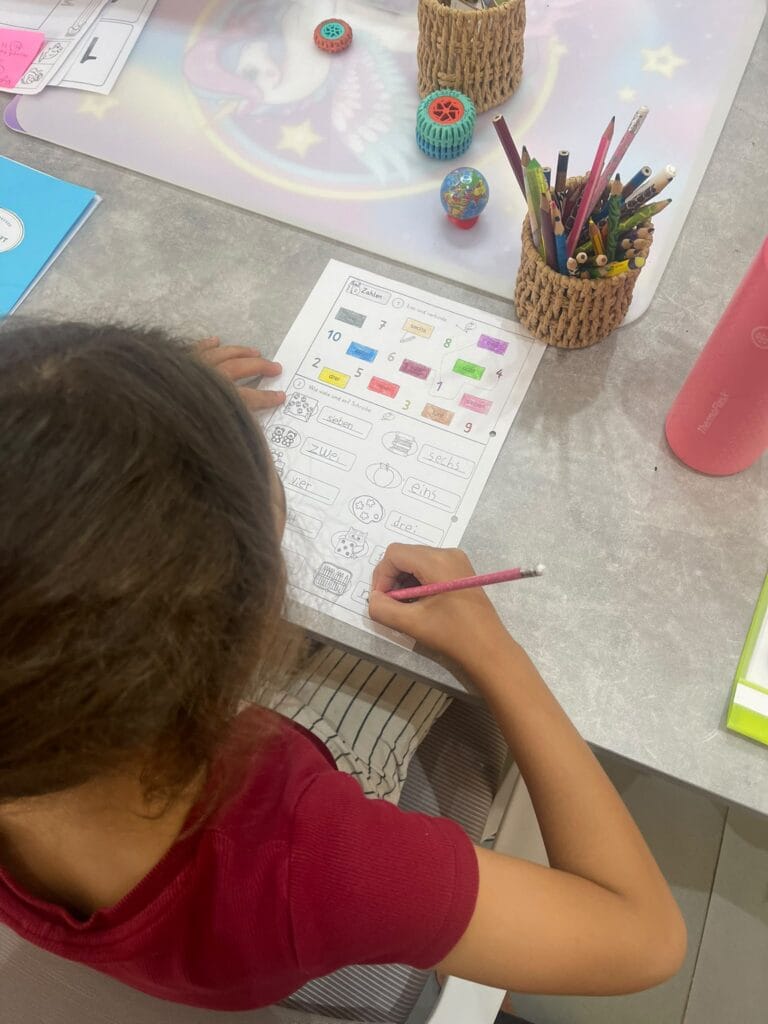 A child writing German numbers on a colourful worksheet in a German lesson at Studyfreunde in Accra