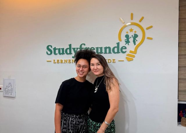 Two women in front of the Studyfreunde logo at the German language school in Airport West, Accra